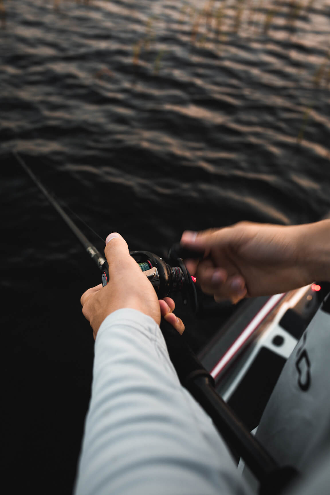 A pair of hands holding onto a fishing pole and their line is in the water.