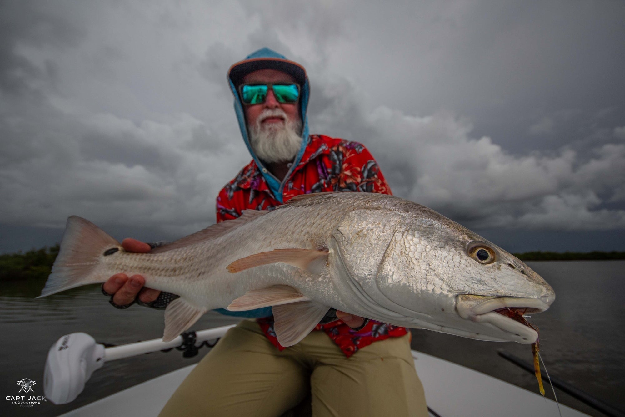 A fisherman is seated on a boat and holding onto a redfish.
