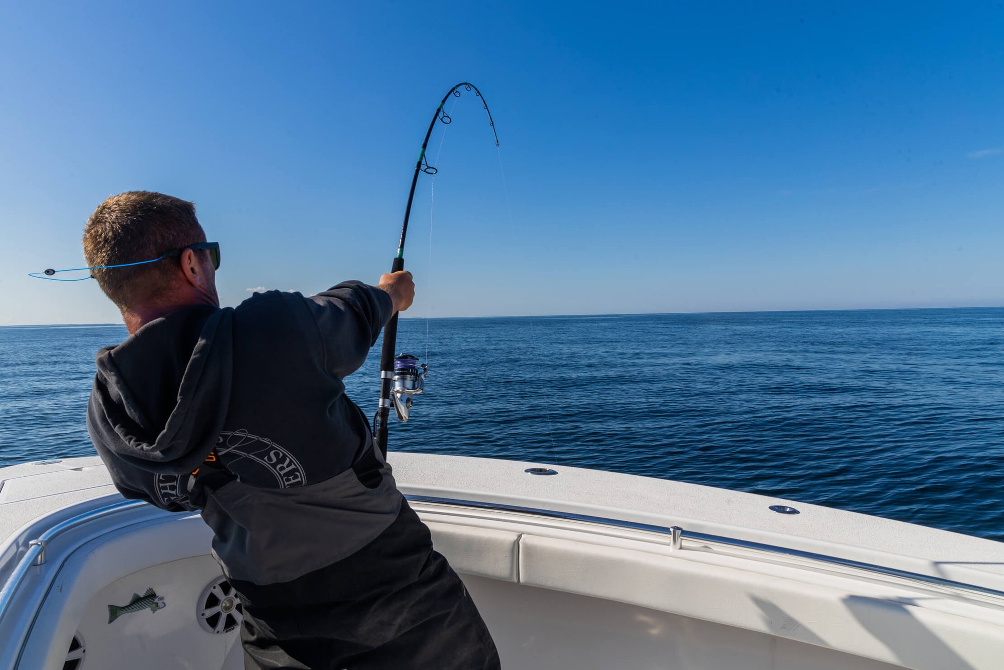 An angler is standing on a boat and reeling in his fishing line