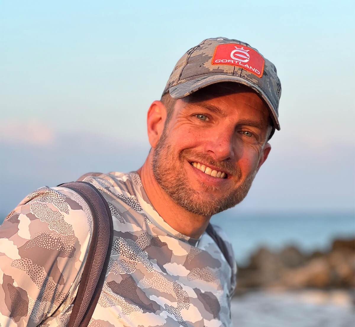 Mark Wechsler is smiling at the camera with a Cortland hat on and a white cameo shirt 