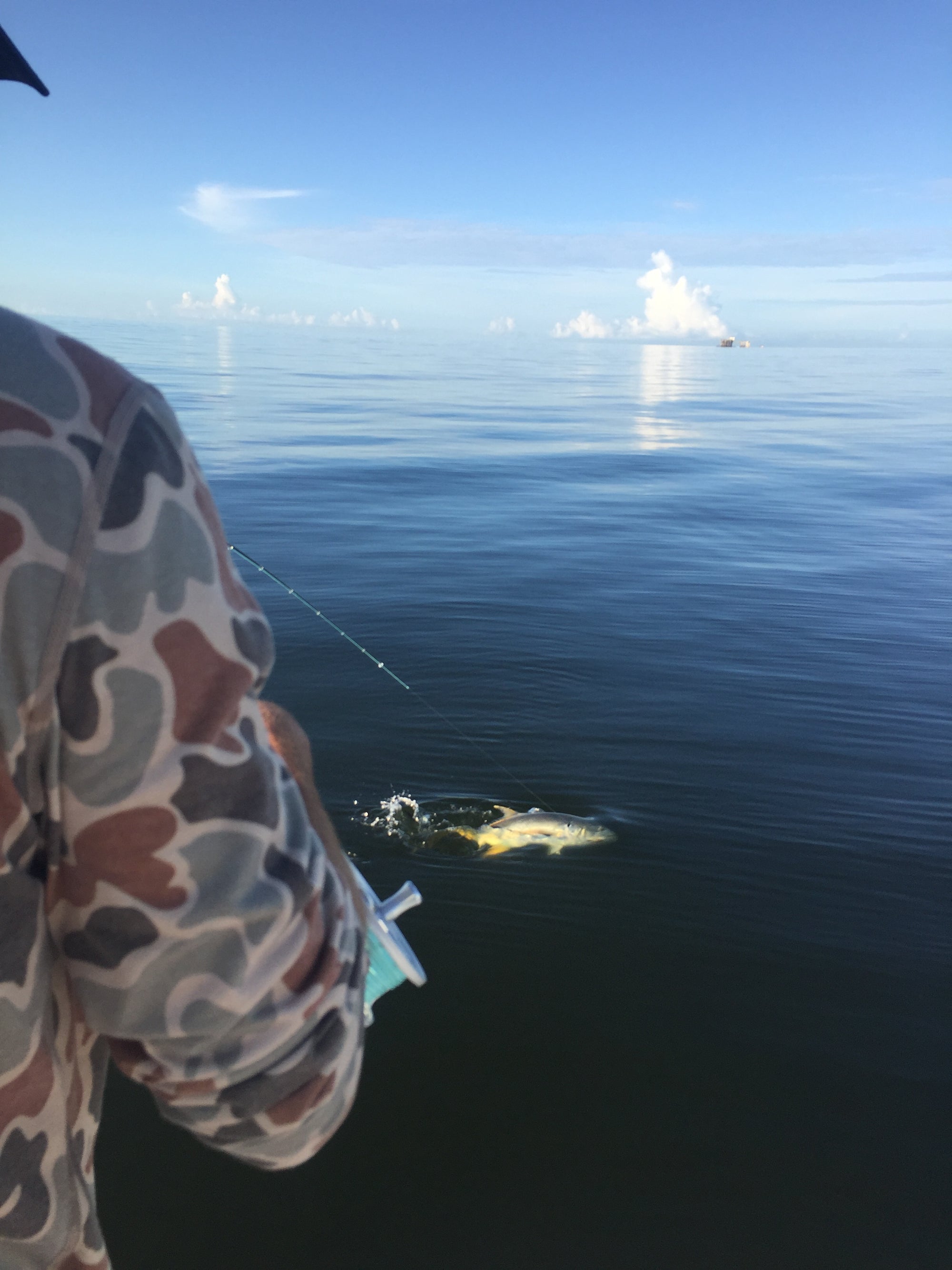 An angler with their back to the camera has a fish caught onto their fishing line. 