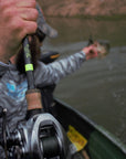 An angler is on a boat while holding a fish with one hand and their pole with another. 