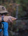 A angler in a light blue shirt holding onto a fly rod with his right hand. 